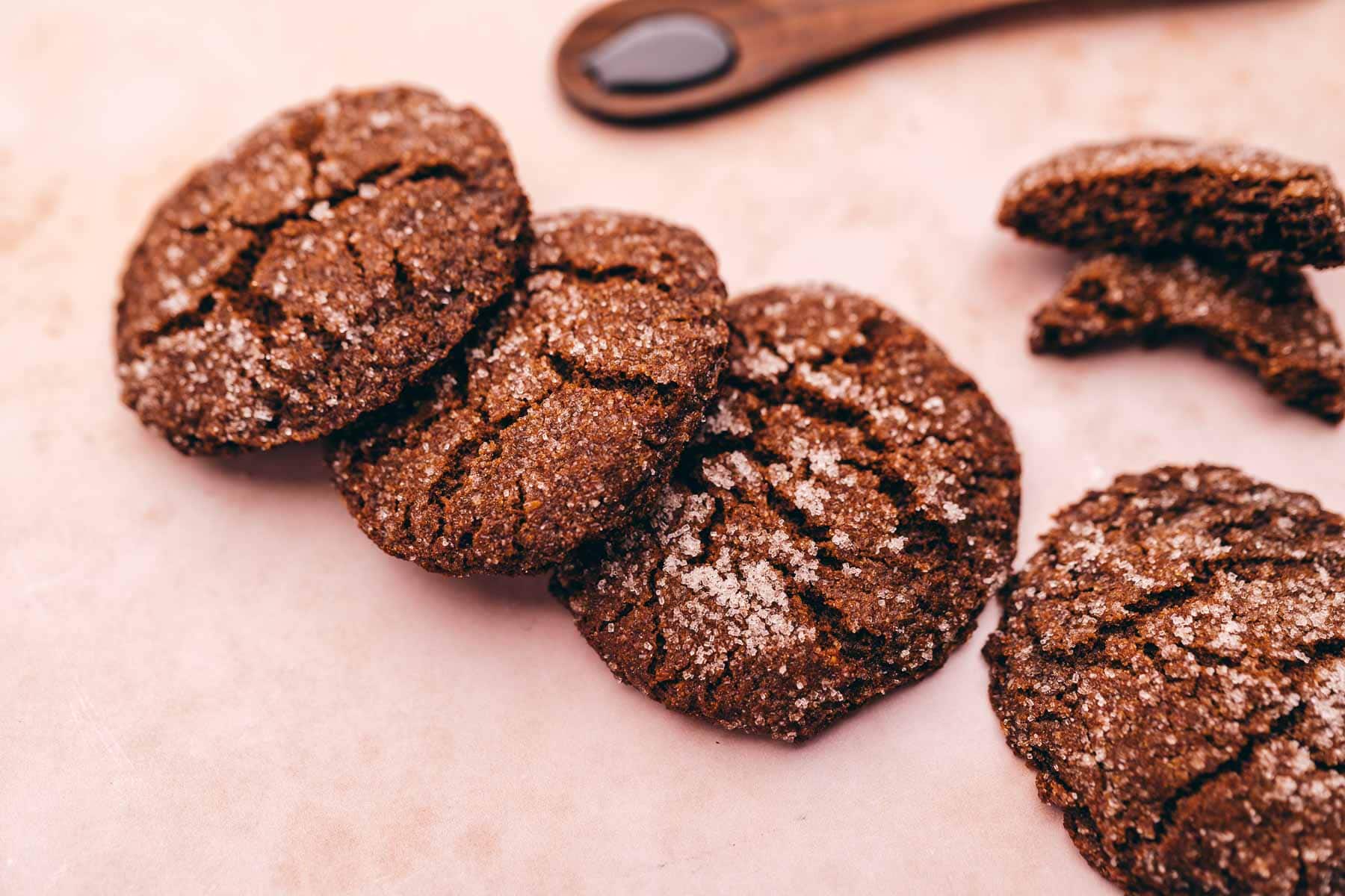 A group of gluten-free chocolate molasses cookies on a pink surface with a spoon.