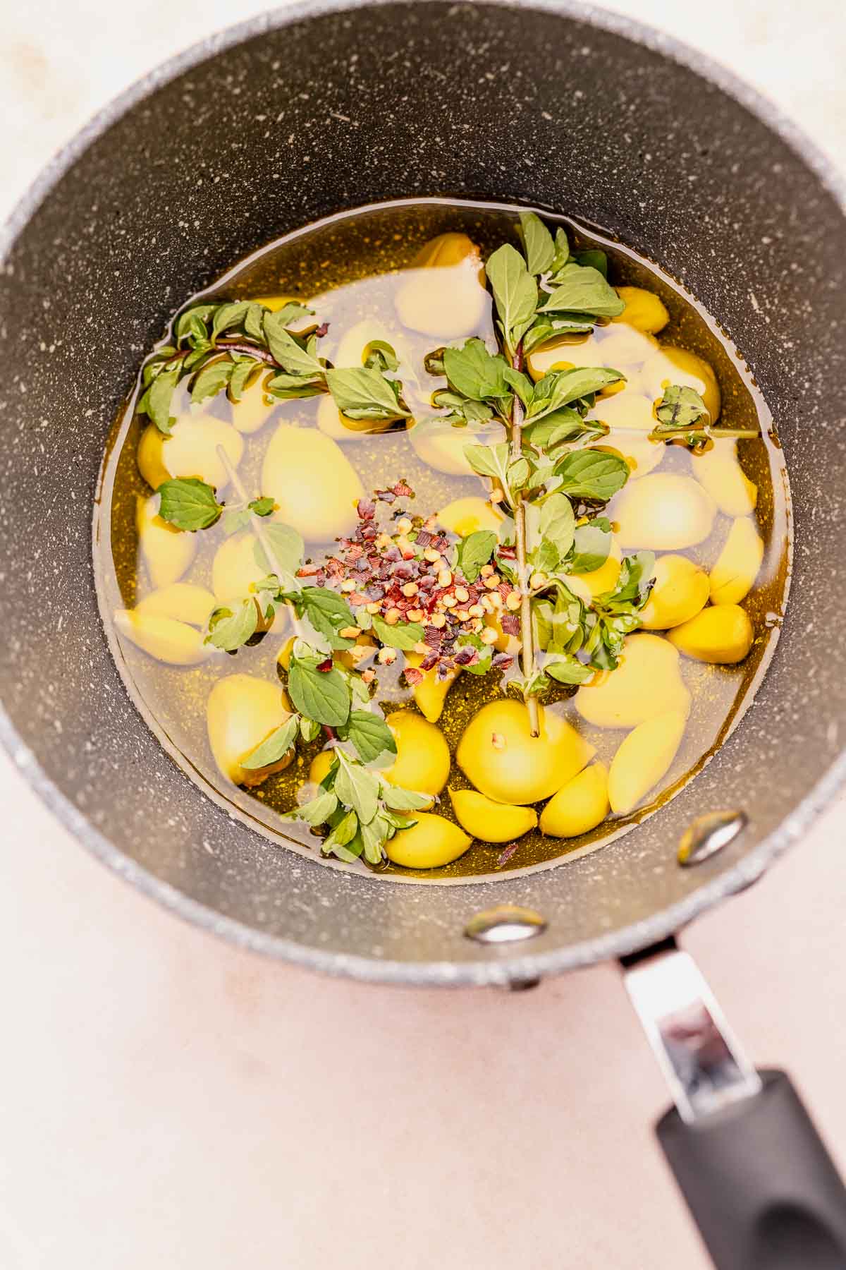 A frying pan filled with garlic confit, lemons, and herbs.