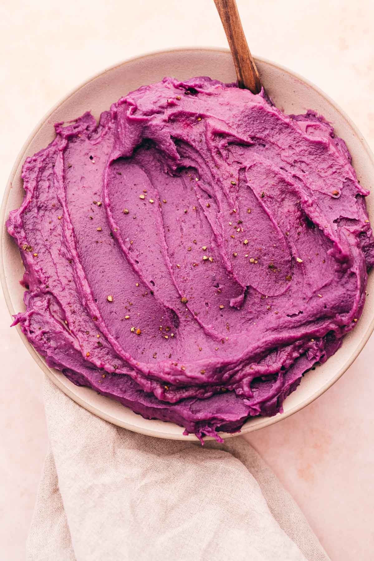 Mashed purple sweet potatoes hummus in a bowl with a wooden spoon.