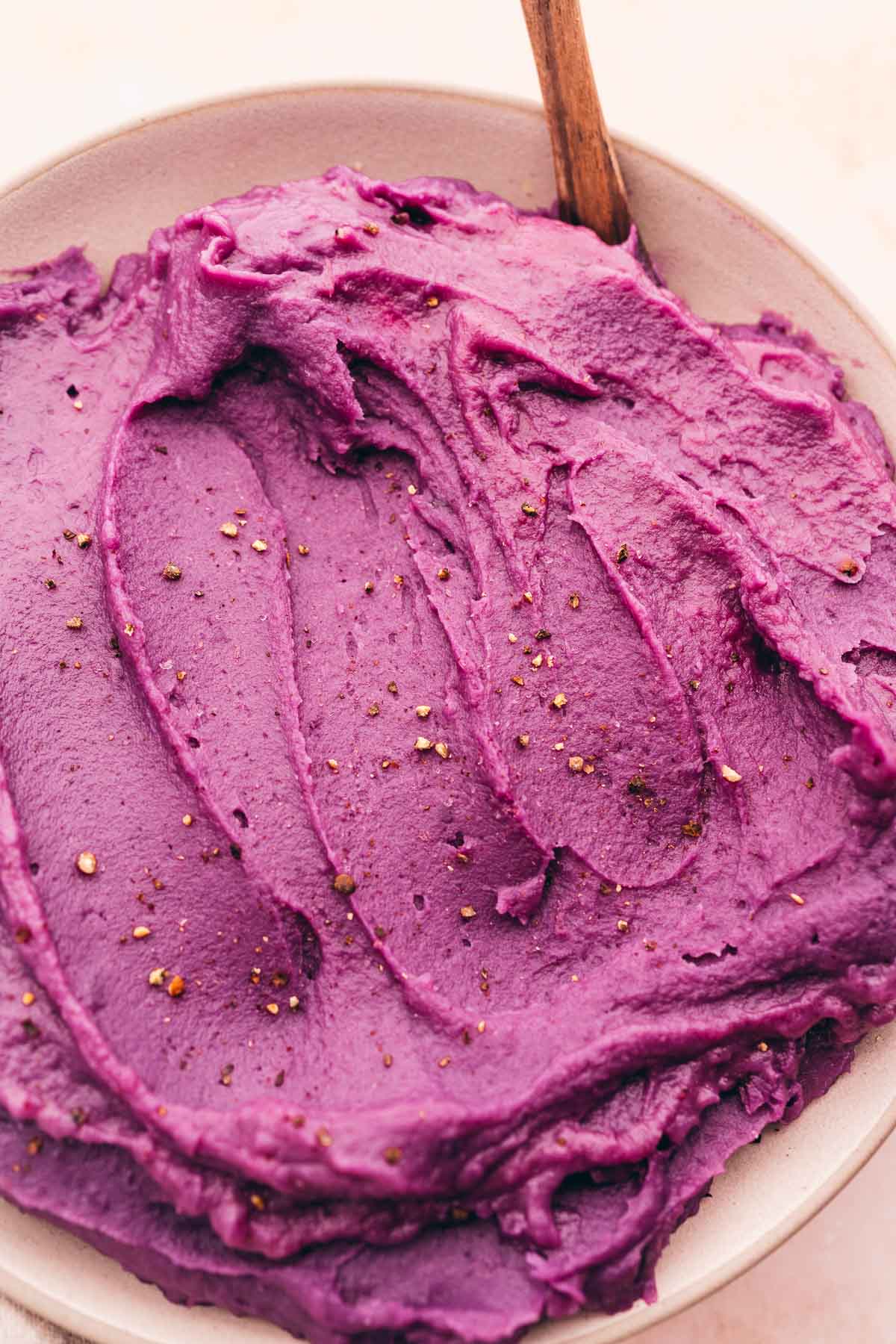 Mashed purple sweet potatoes hummus in a bowl with a wooden spoon.