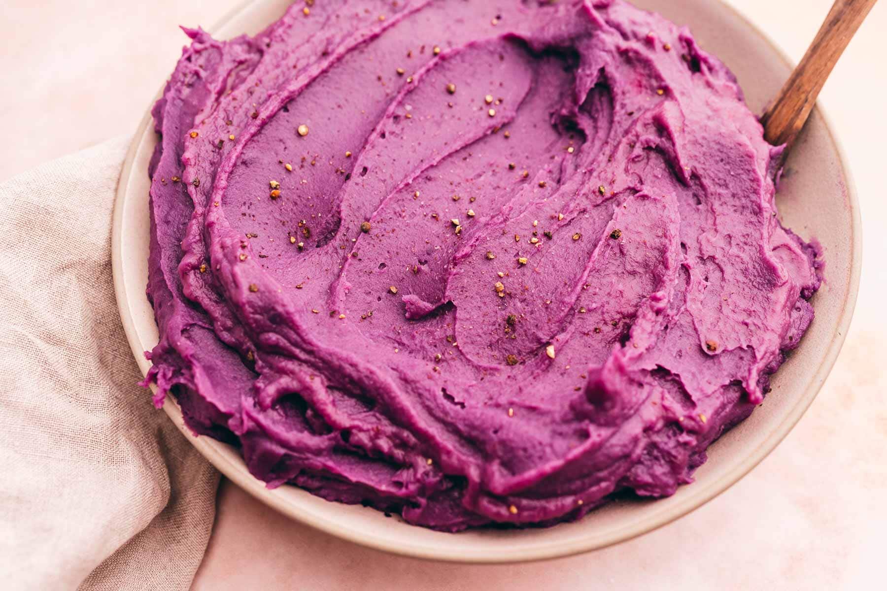 Mashed purple sweet potatoes in a bowl with a wooden spoon.