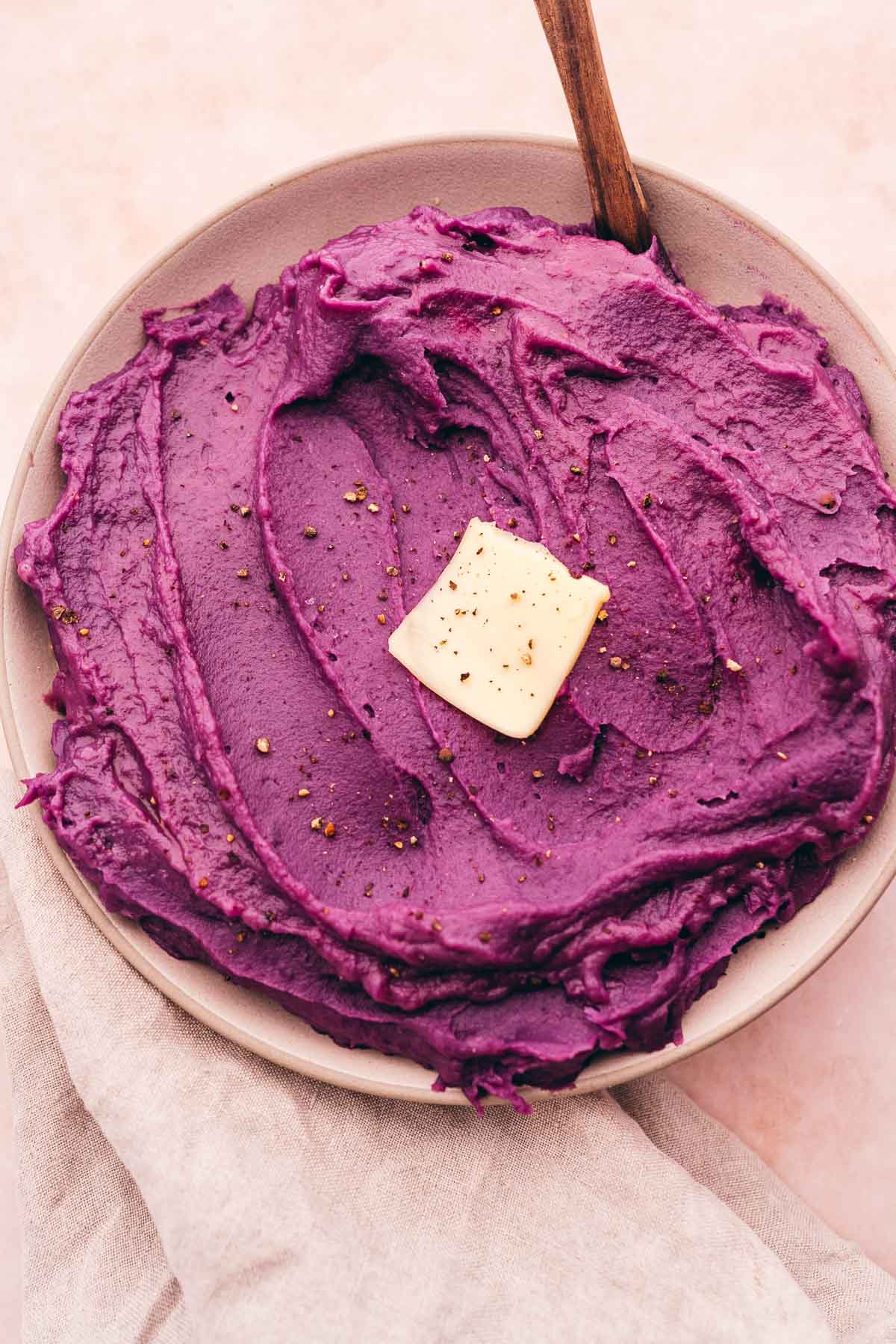 Purple mashed sweet potatoes on a plate with a wooden spoon.