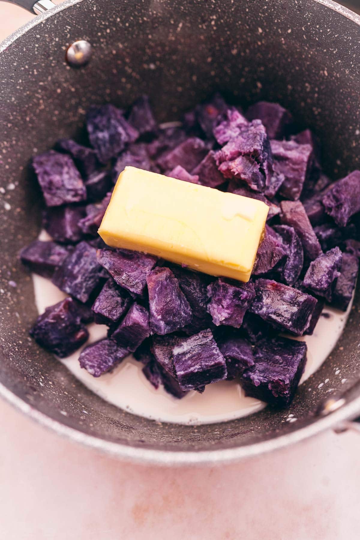 Mashed purple sweet potatoes and butter in a pan.