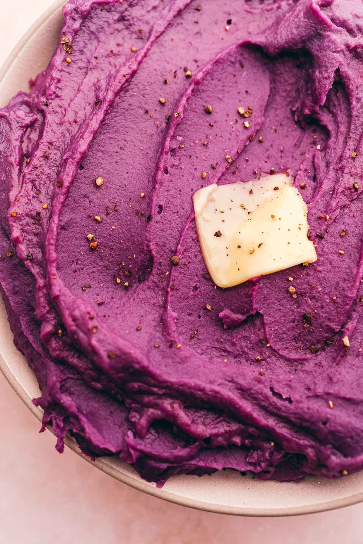 A bowl of mashed purple sweet potatoes with a pat of butter on top.