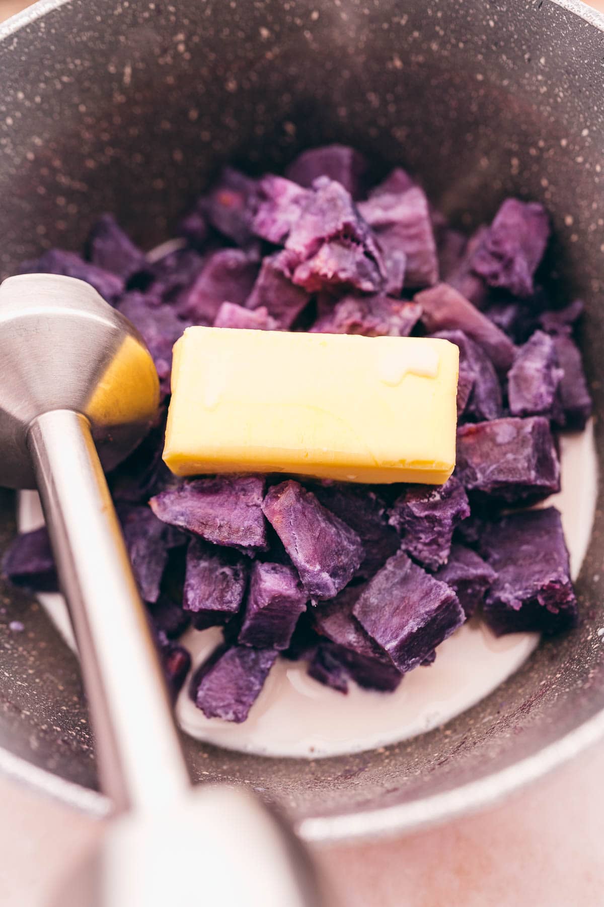 Mashed purple sweet potatoes and butter in a pan.