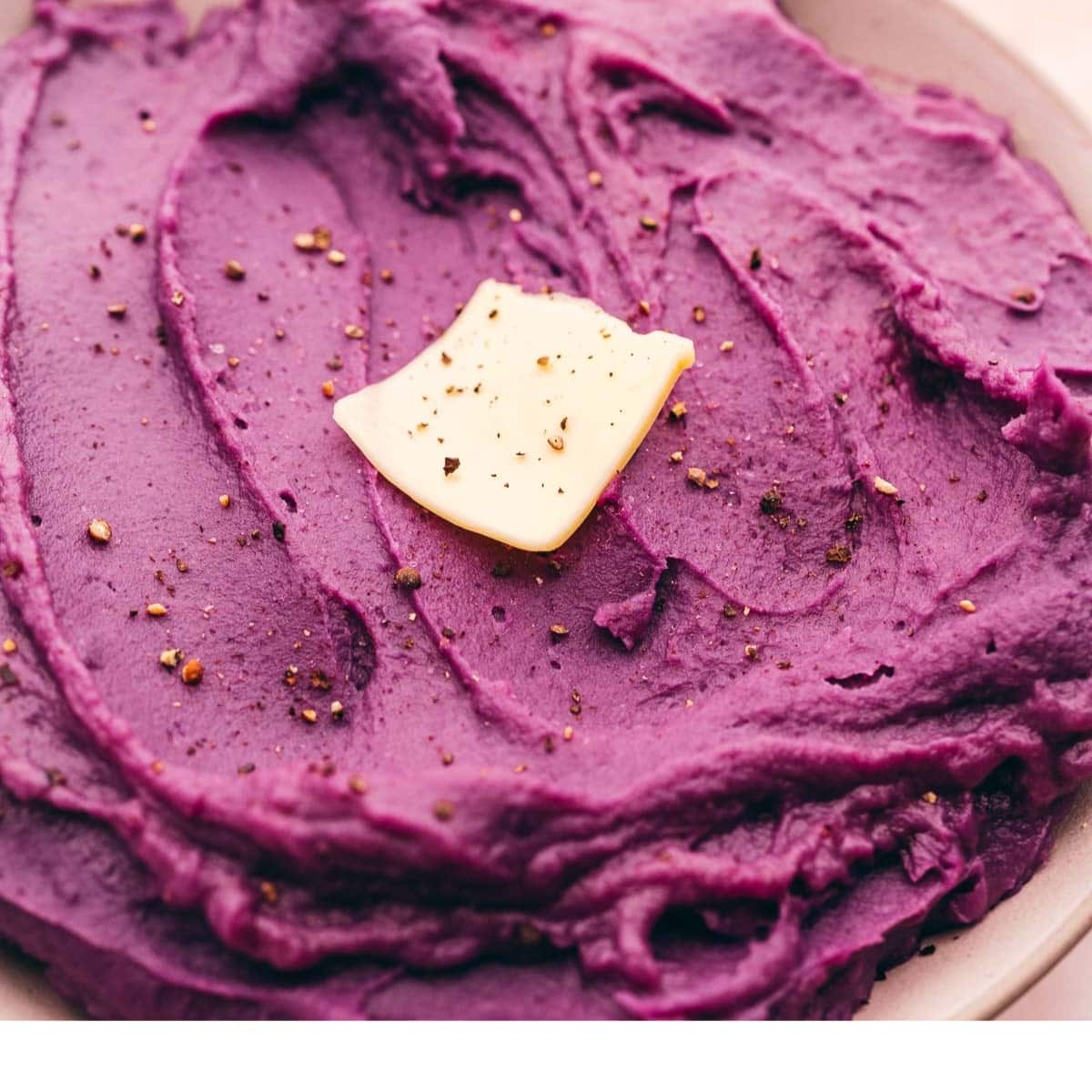 A bowl of purple mashed potatoes with a butter on top made from mashed purple sweet potatoes.