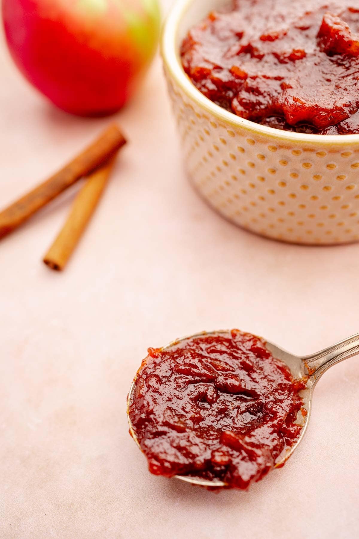 A spoon with a bowl of slow cooker apple butter.