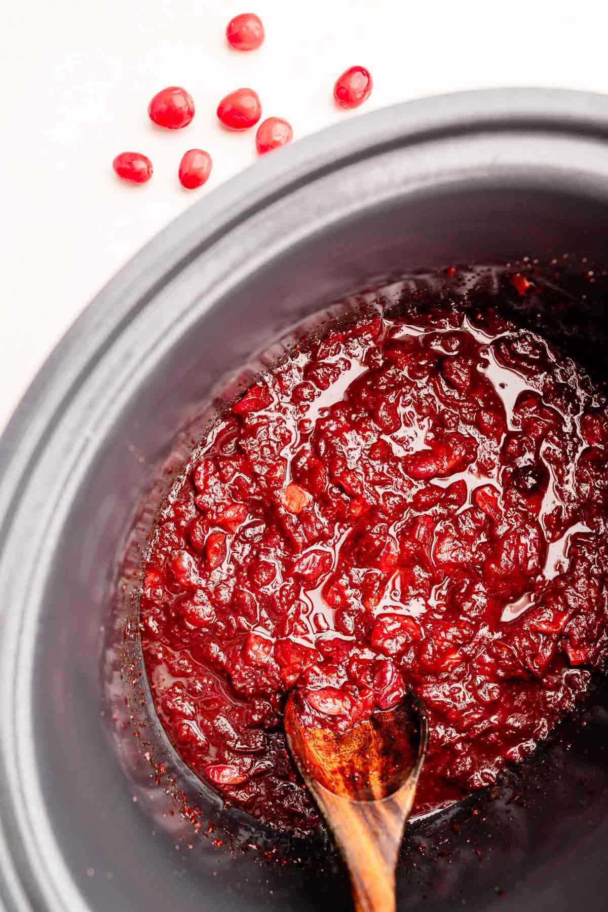 Slow Cooker Cranberry Sauce: Create delicious cranberry sauce effortlessly using a slow cooker and a wooden spoon.