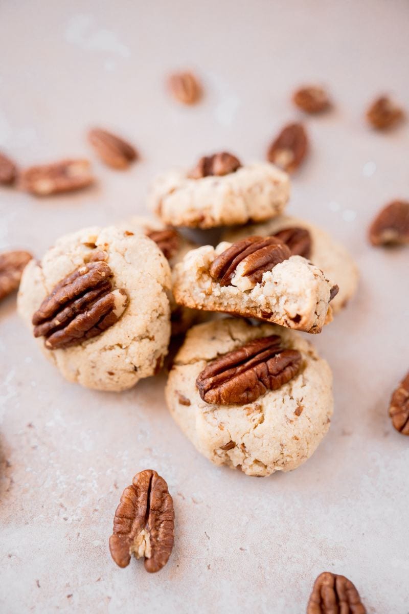 Gluten-free pecan sandies cookies with pecans on a white surface.