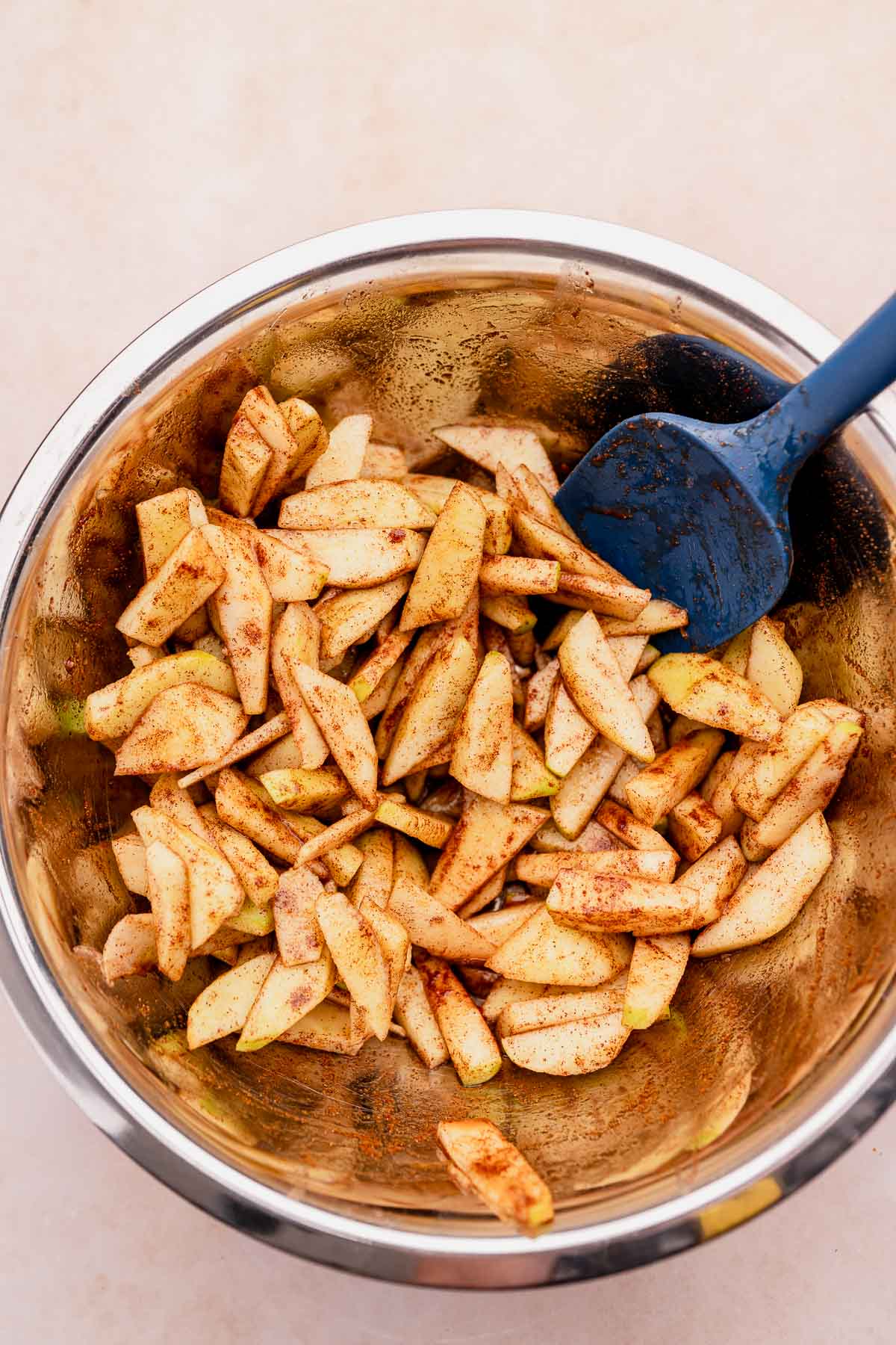 Gluten-free apple slices in a metal bowl with a blue spatula served alongside an apple crisp.