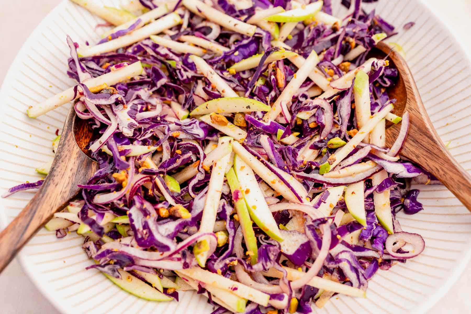 Red cabbage and apple slaw in a bowl with wooden spoons.