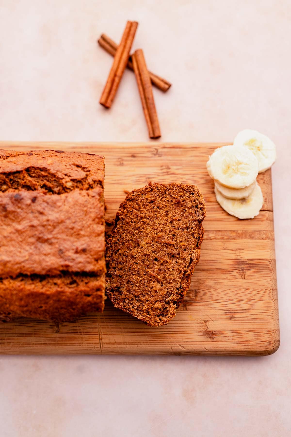 A delicious slice of oat flour banana bread is delicately placed on a rustic wooden cutting board.