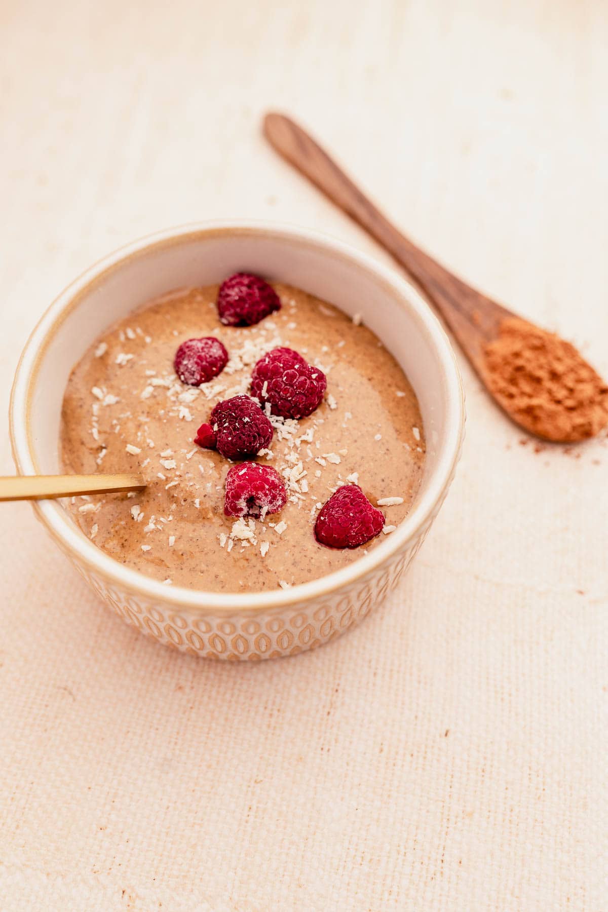 A bowl of oatmeal with raspberries, blended chocolate chia pudding, and a spoon.
