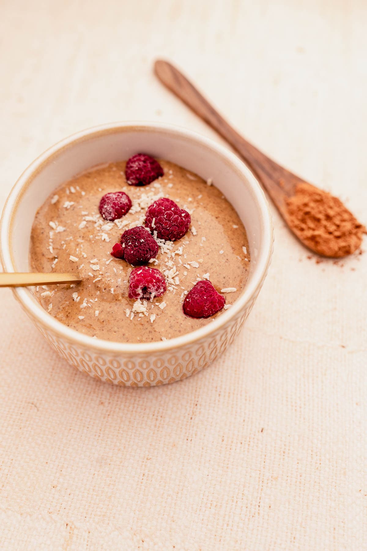 A bowl of oatmeal with raspberries and a spoon.
