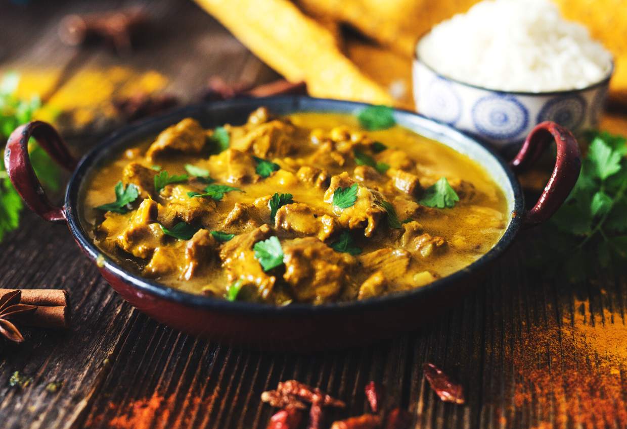 A bowl of curry with different types of meat and a blend of aromatic spices on a rustic wooden table.