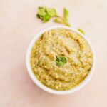 A bowl of pesto dip with oregano leaves.