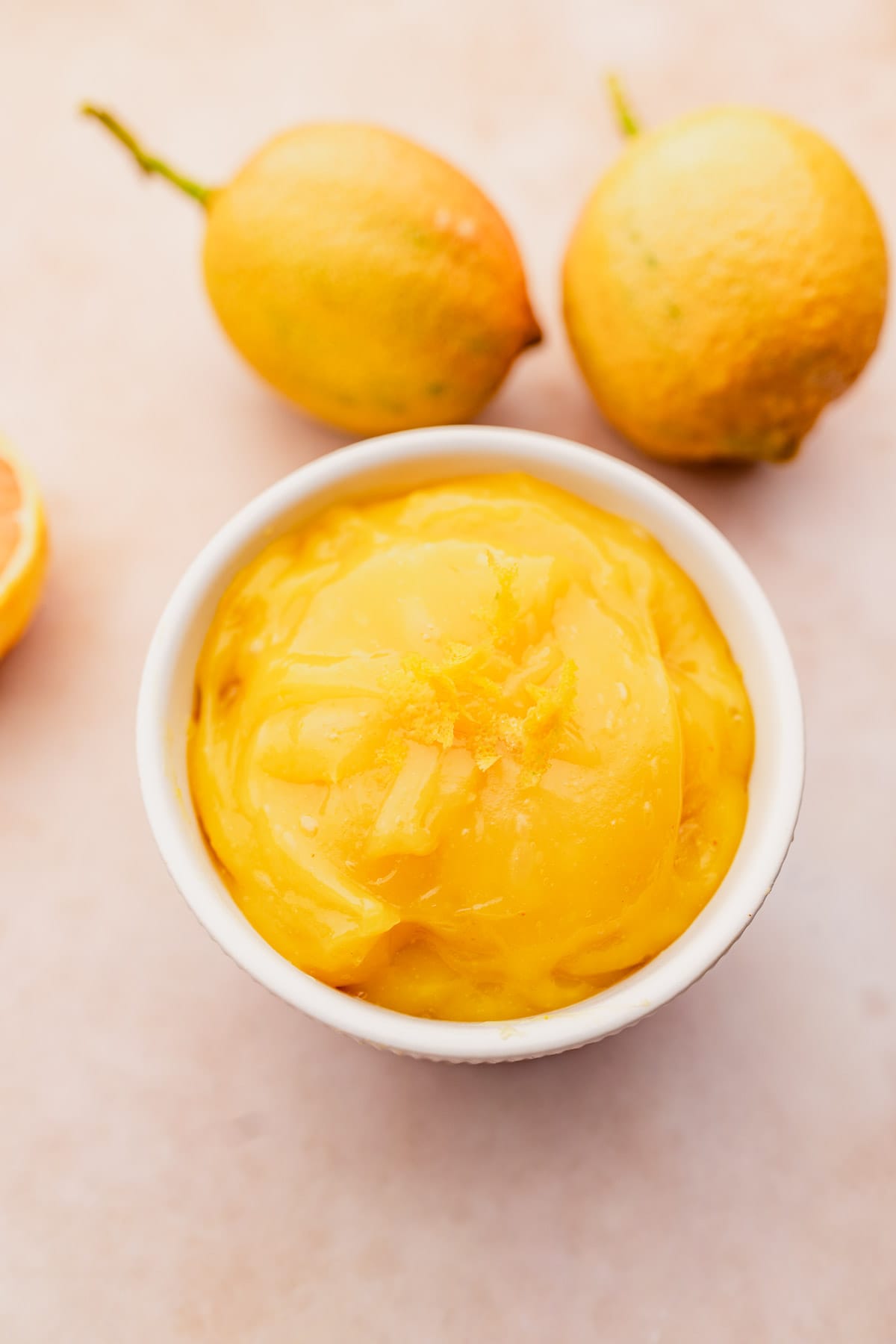 A bowl of vegan lemon curd on a table next to some oranges.