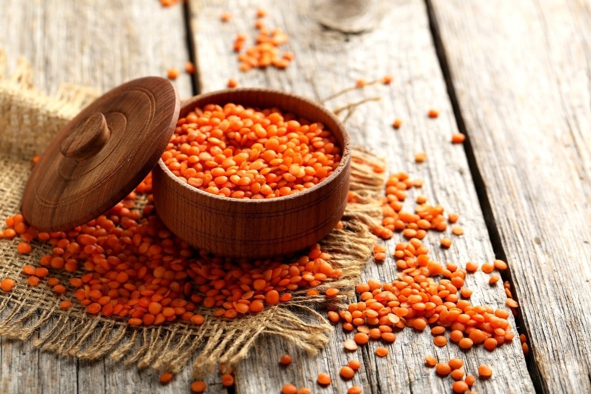 Orange lentils in a wooden bowl on a wooden table.