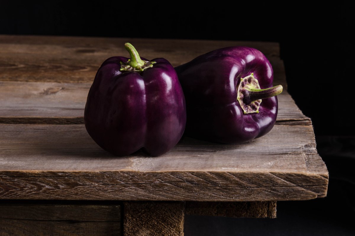 Two purple peppers on a wooden table.