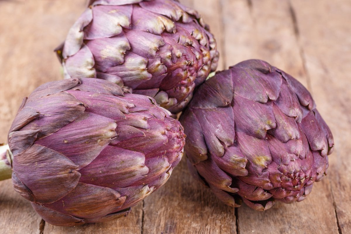 A group of artichokes on a wood surface.