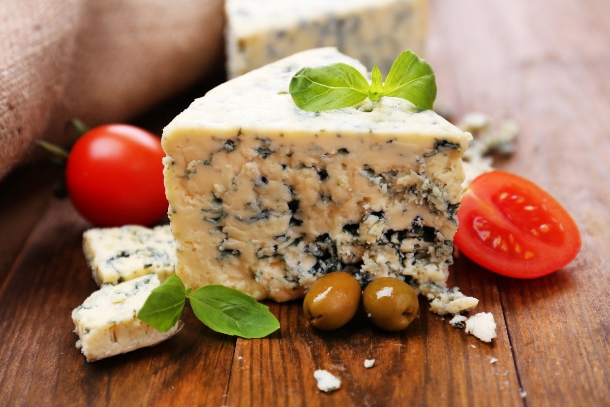 Blue cheese with tomatoes and olives on a wooden table.