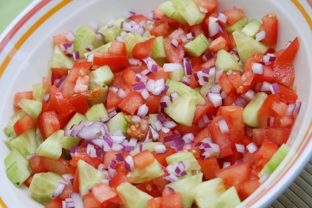 A bowl full of chopped tomatoes, onions, and cucumbers.