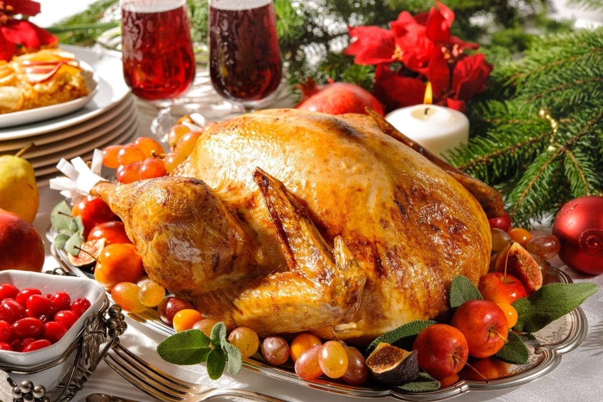 A turkey is sitting on a platter with fruit and wine.