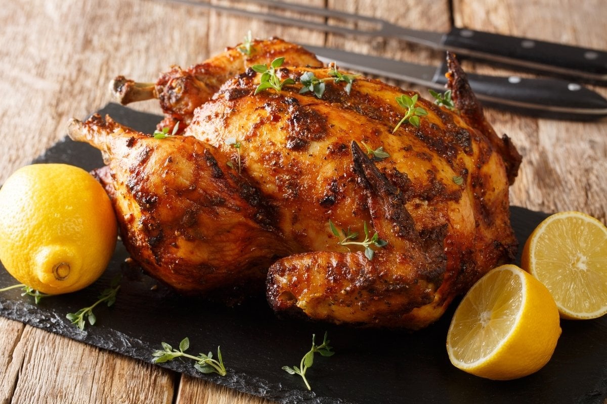 A roasted chicken with lemons and herbs on a slate.