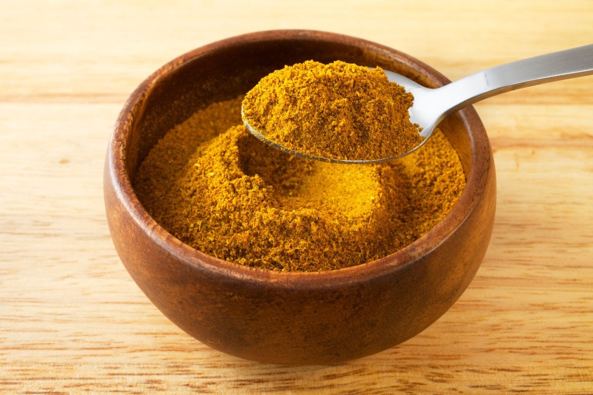 A spoonful of tumeric powder in a wooden bowl.