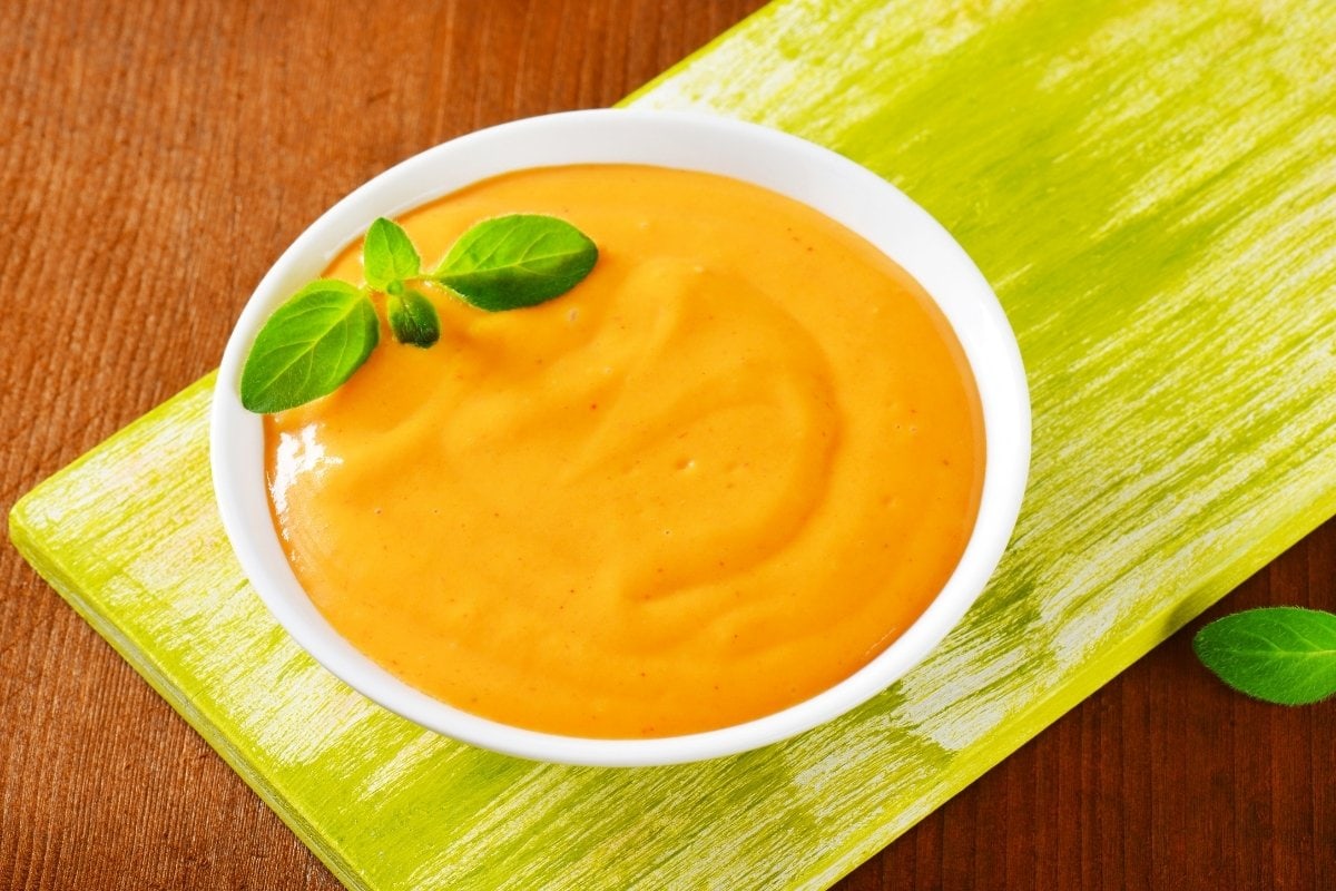 A bowl of orange sauce on a wooden table.