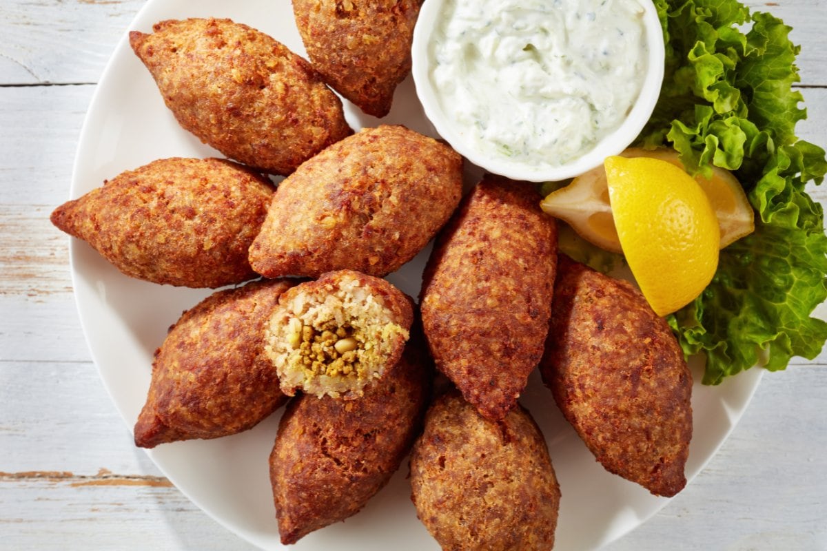 Kebabs with tzatziki sauce on a white plate.