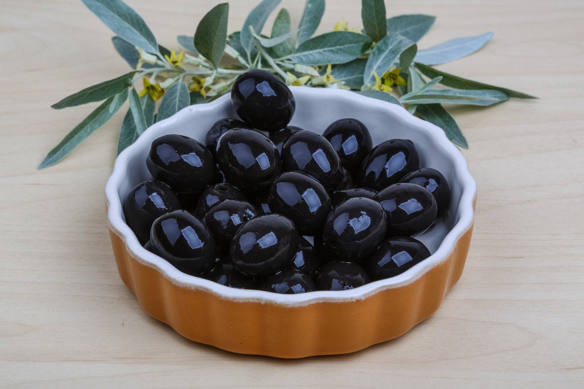 Black olives in a bowl with eucalyptus leaves.
