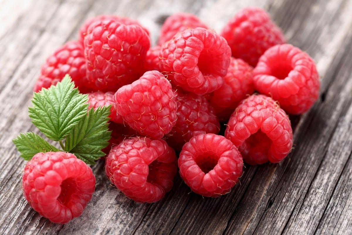 A pile of raspberries on a wood surface.