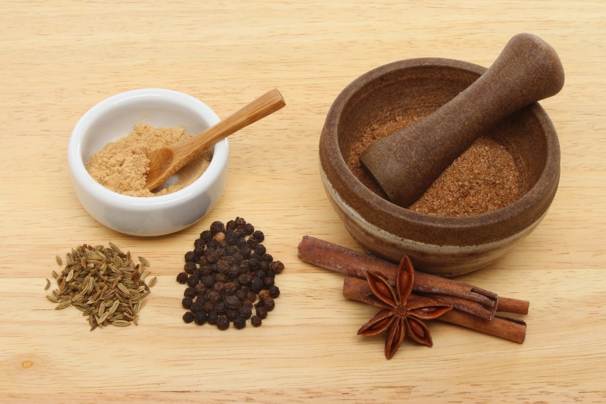 A mortar and pestle with spices and herbs on a wooden table.