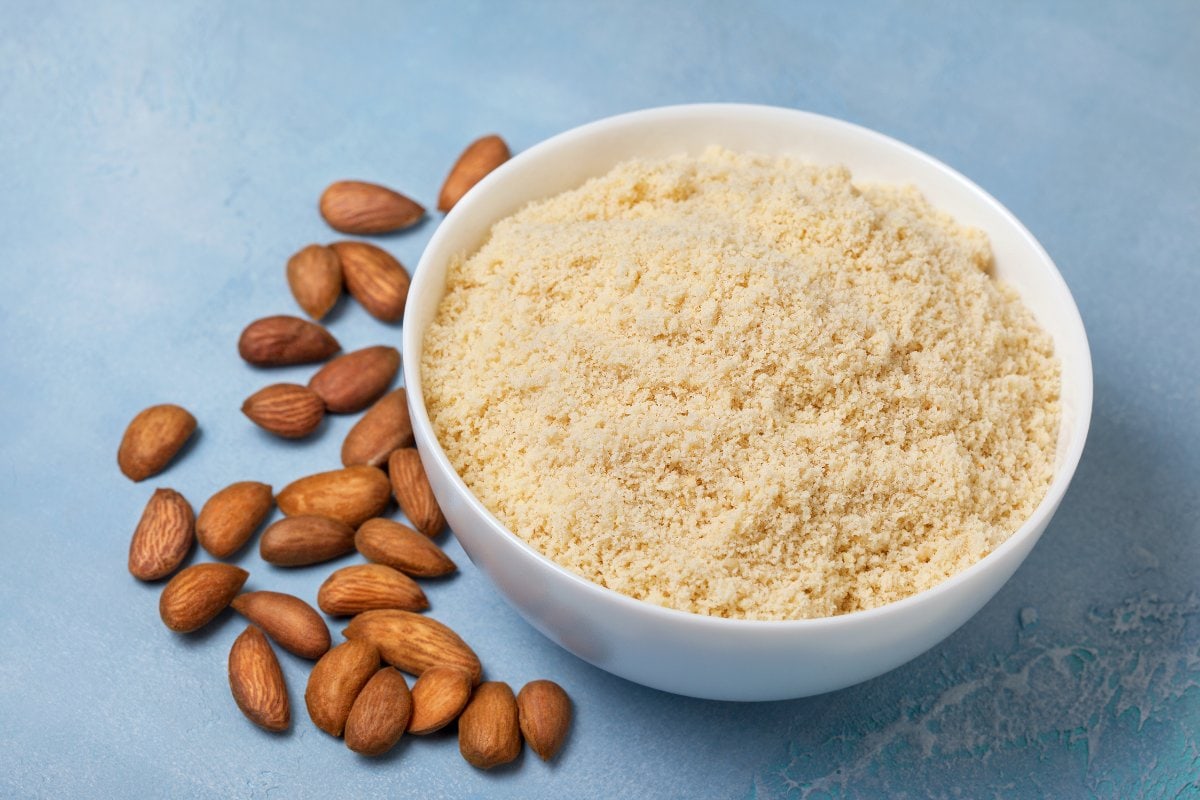 Almond flour and almonds in a bowl on a blue background.
