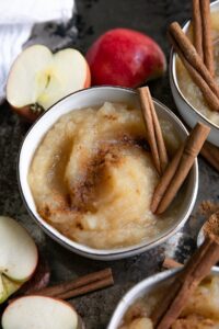 Applesauce in bowls with cinnamon sticks and apples.