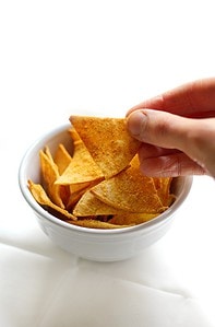 A hand reaching into a bowl of tortilla chips.