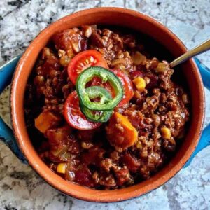 Chili in a blue bowl with tomatoes and jalapenos.