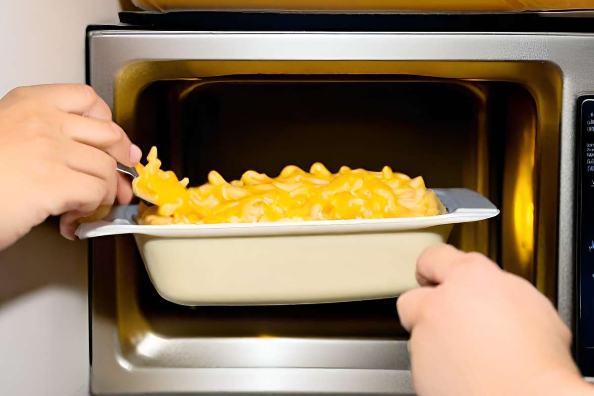 A person putting macaroni and cheese into a microwave.