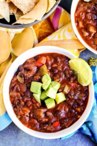Two bowls of black bean chili with guacamole and tortilla chips.
