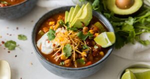 A bowl of mexican chili with avocado and lime.