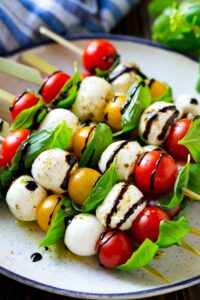 Skewers with tomatoes, mozzarella and basil on a plate.