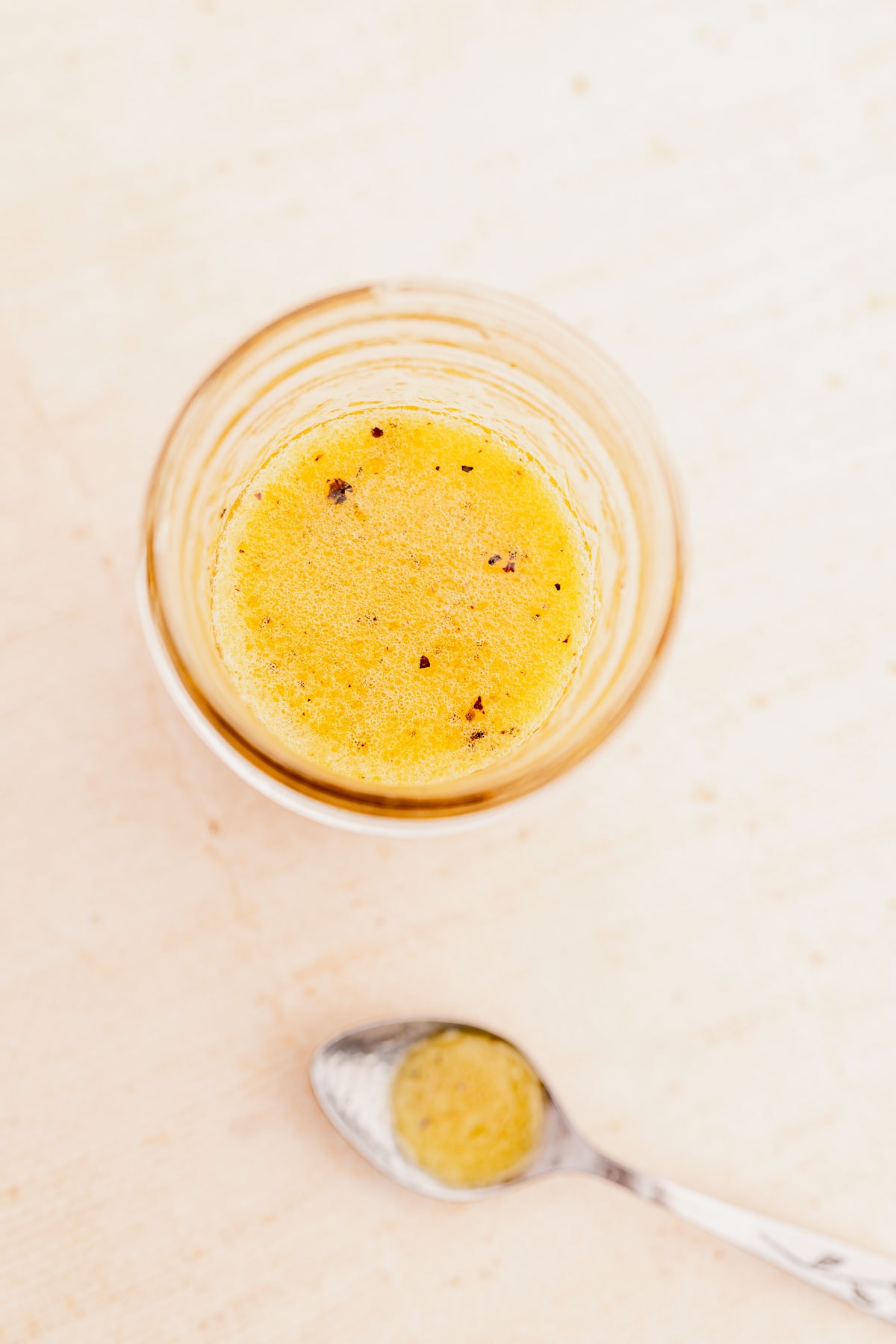 An open jar of citrus vinaigrette on a tan table.