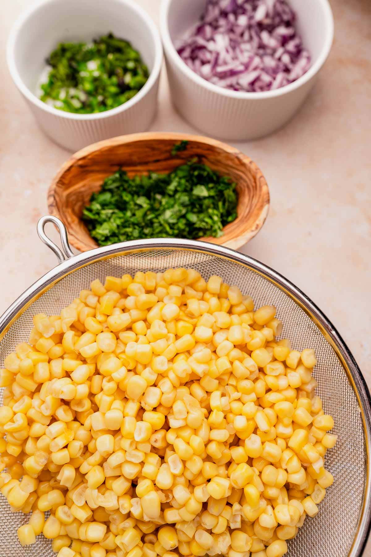 A savory mix of chipotle corn salsa with onions and other ingredients in a sieve.