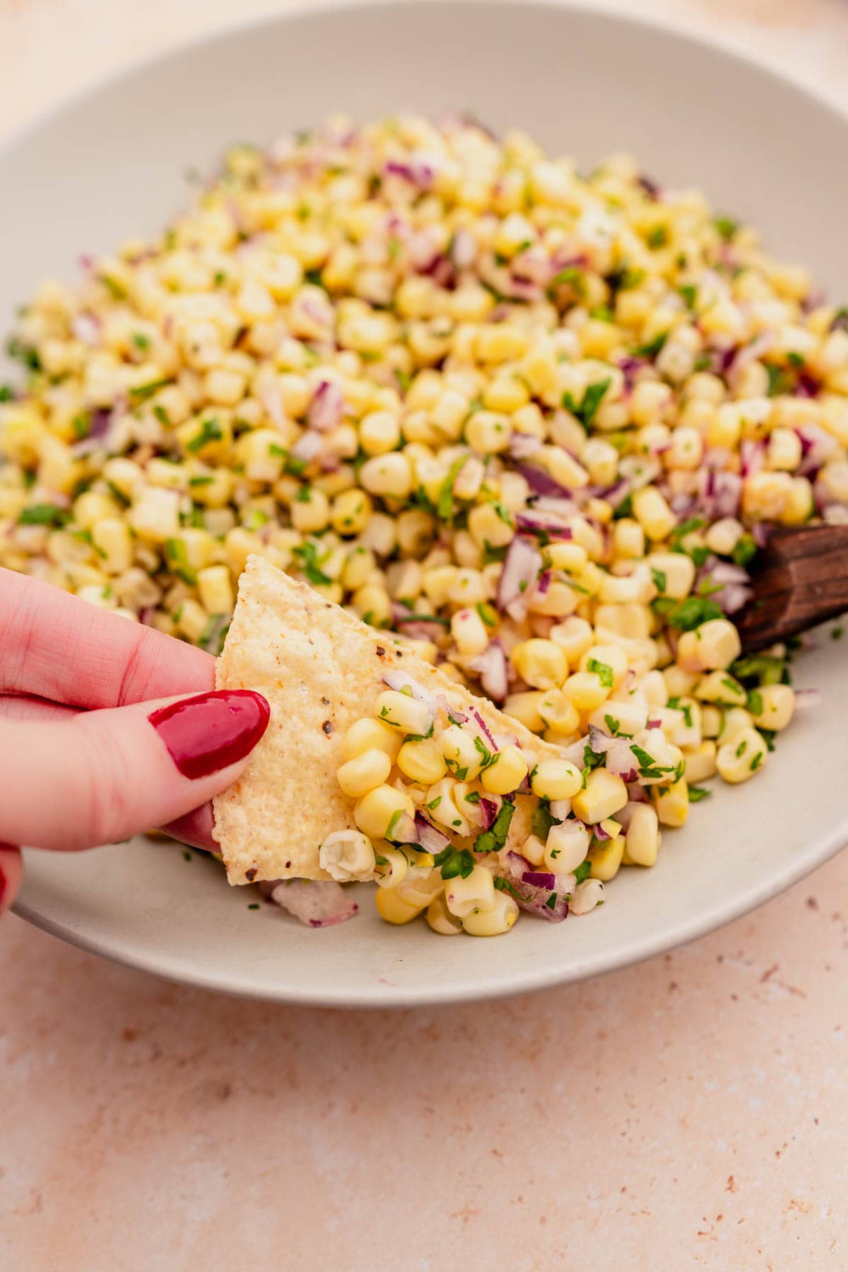 A hand is dipping a tortilla into a bowl of chipotle corn salsa.