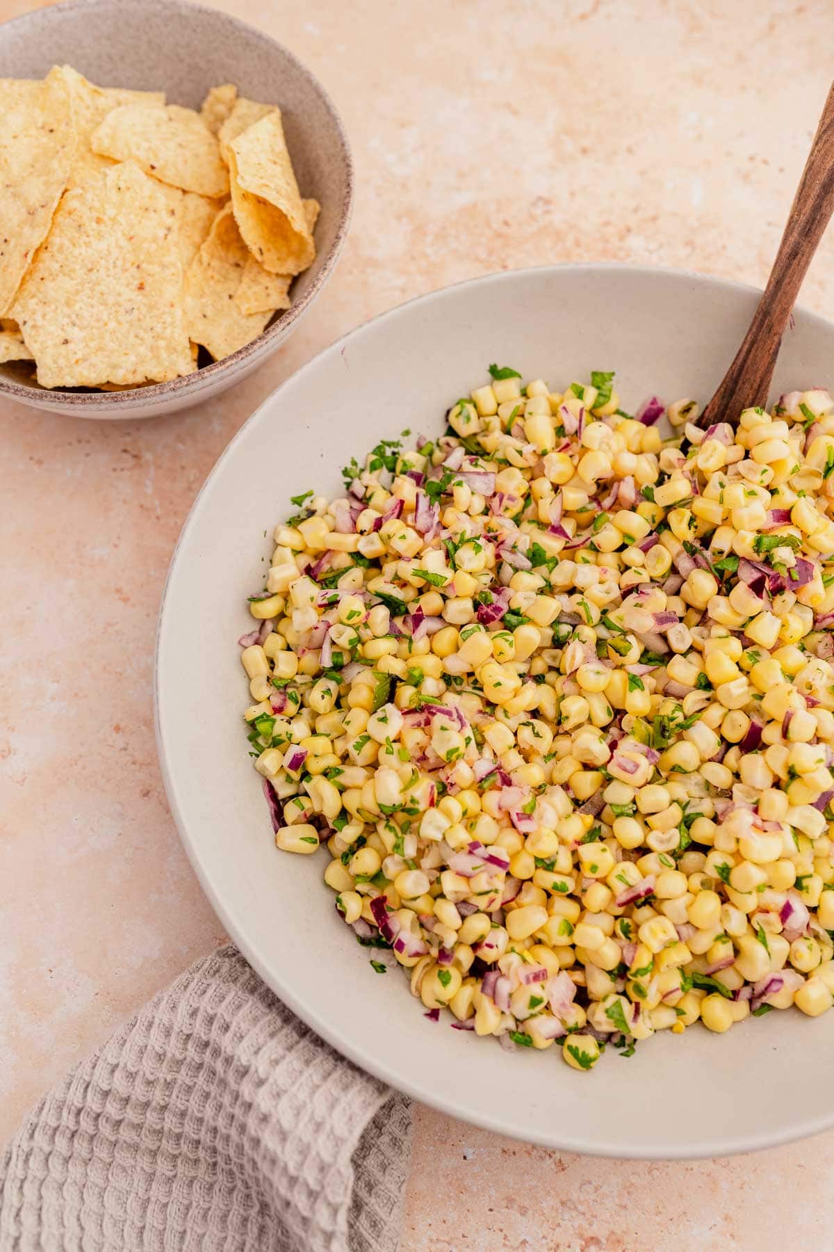 A bowl of chipotle corn salsa with tortilla chips and a wooden spoon.