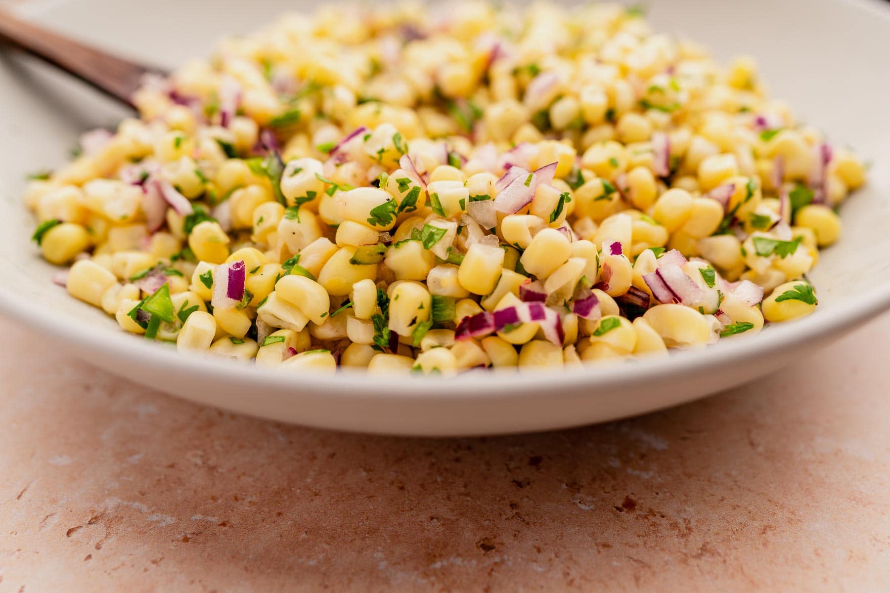 Corn salad in a white bowl with a wooden spoon, topped with chipotle corn salsa.