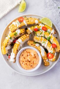 Corn on the cob with dipping sauce on a white plate.