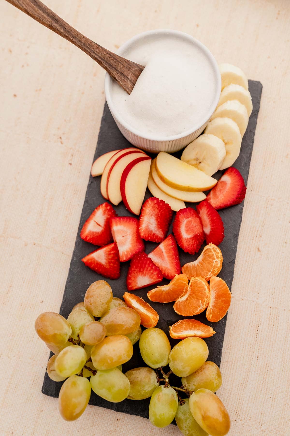 A platter of fruit and yogurt with a fruit dip on a slate board.