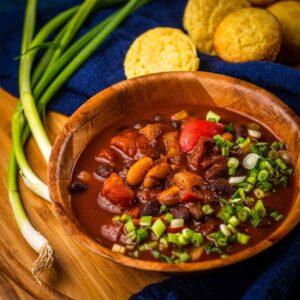 A bowl of chili with cornbread on a wooden table.